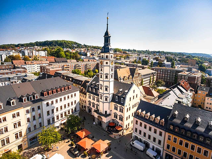Panoramablick von oben auf den Rathausturm auf dem Marktplatz in Gera, umgeben von strahlendem Sonnenschein und einem klaren blauen Himmel